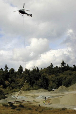 A helicopter hoists a power pole into the air at the Glacier gravel pit.