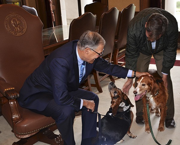 Washington Governor Jay Inslee (seated) pets Tillie as islander B.J. Duft stands over her and Phoebe looks on. The three were invited to Inslee’s office Thursday.