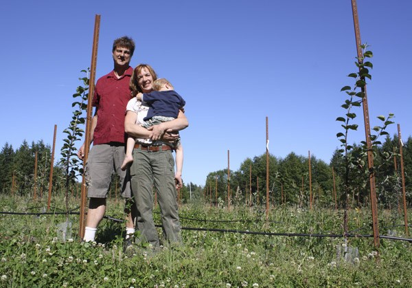 Wes and Laura Cherry stand in their orchard of young cider apple trees. Laura holds the couple's 3-year-old son Quentin.
