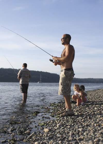 Islander Joey Pinczes casts his line from Manzanita Beach last week while his children play at the water’s edge.