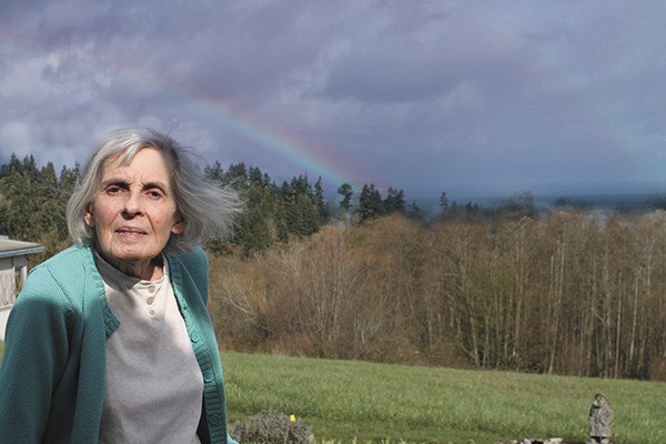 Ina Whitlock stands under a rainbow outside her house.