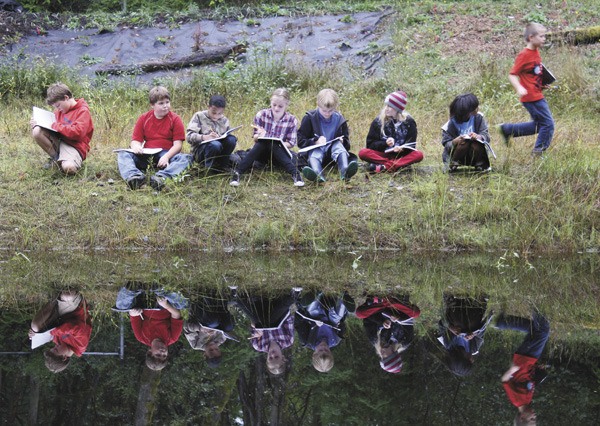Students from Kay Burrell’s fifth-grade class sit next to the detention pond Monday