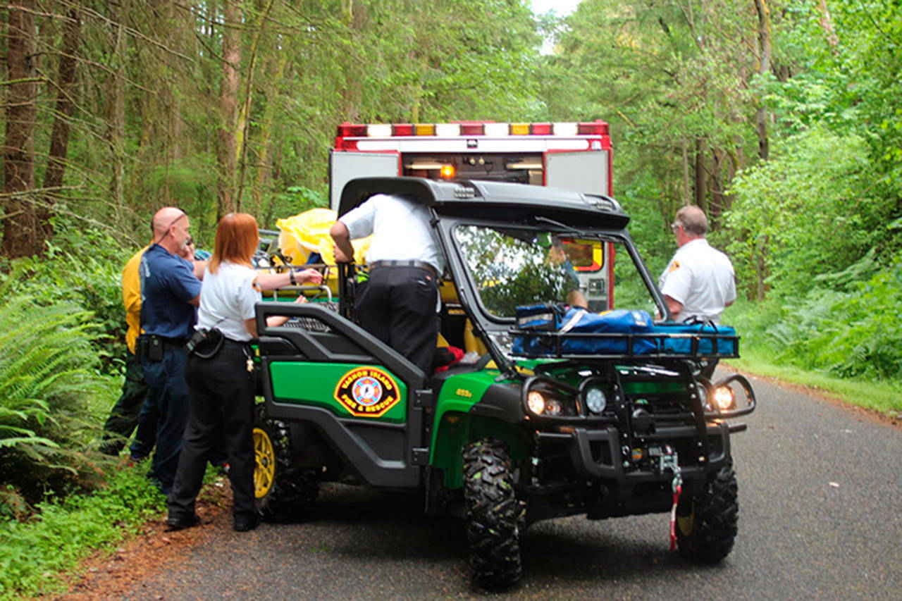 Medic One paramedics and members of Vashon Island Fire & Rescue transfer an injured biker from the district’s Gator to a waiting ambulance on Thursday. (Brigitte Brown Photo)
