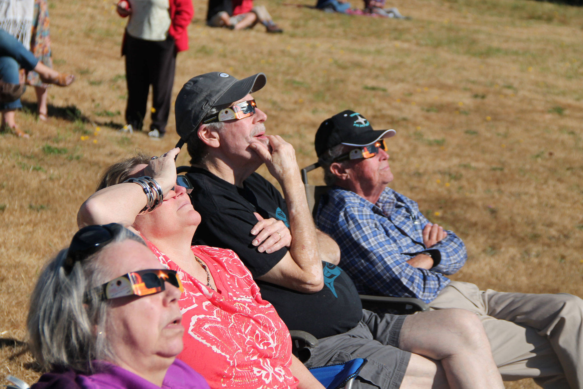 Donning special eclipse glasses, a group of islanders sits in the grass at Sunrise Ridge to watch Monday’s eclipse. (Anneli Fogt/Staff Photo)