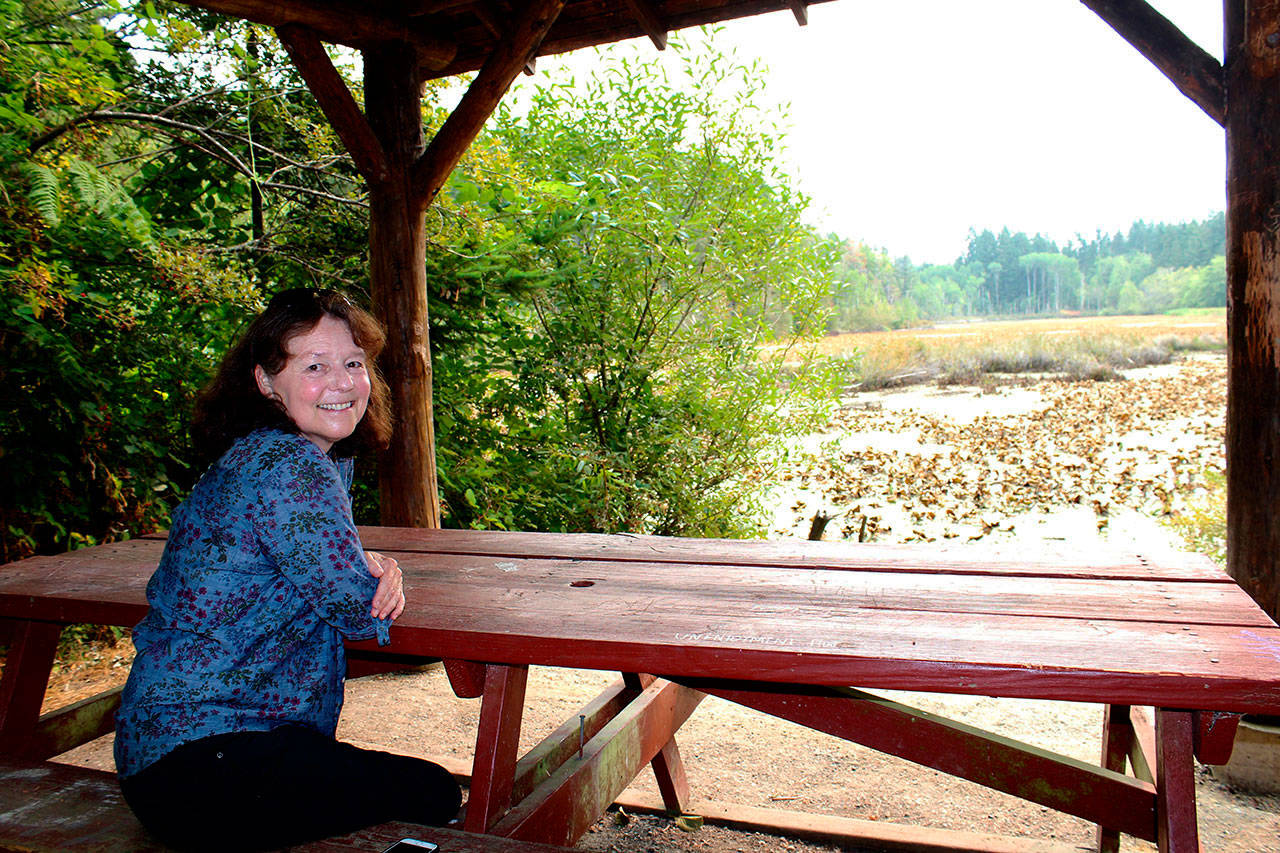 Laurie Bevin Stewart, author of On Fisher Pond: Memories of Bill Fisher and His Gift to Vashon Island,” sits at the pond in the center of Vashon. (Juli Goetz Morser/Staff Photo)