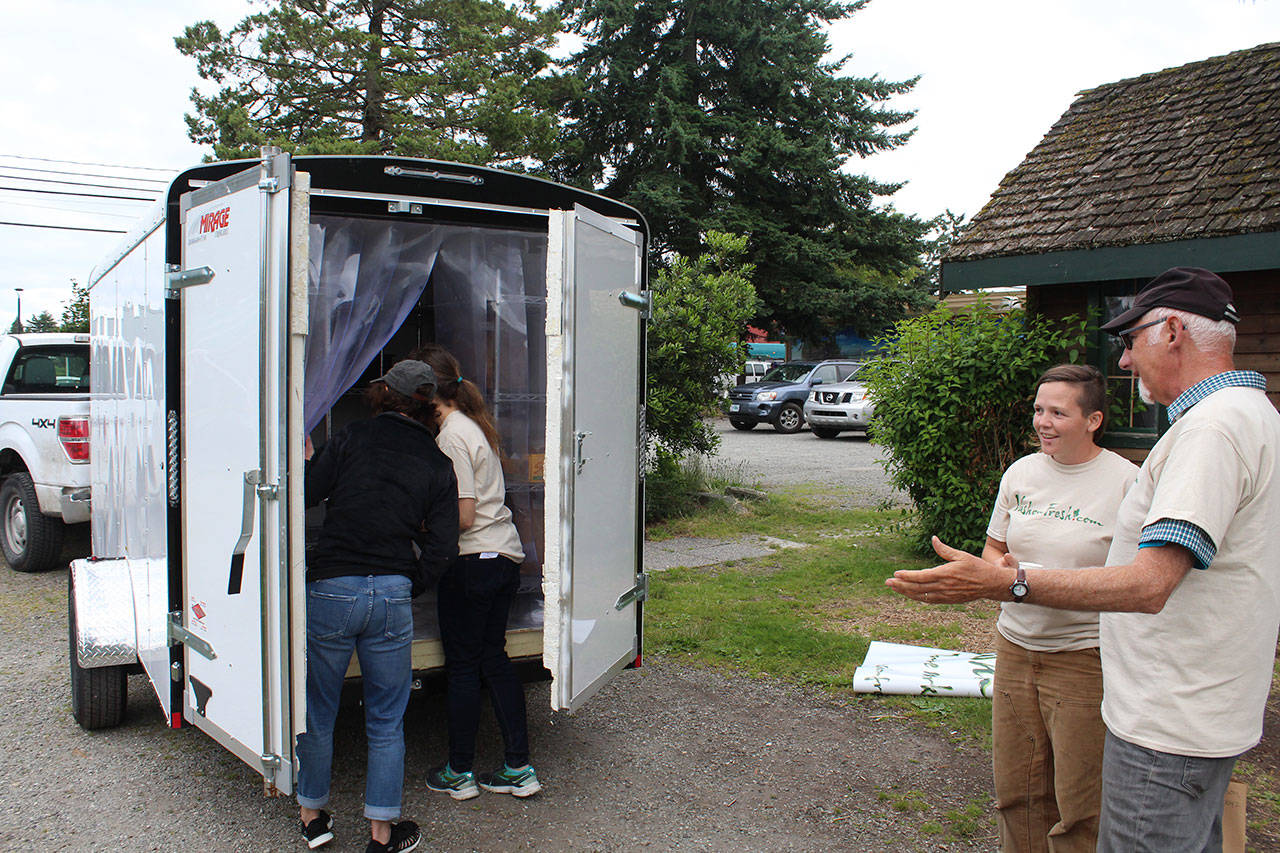 At left, Heidi Hanspetersen (in white) shows Vashon Park District commissioner Lu-Ann Branch the trailer VIGA bought with a grant that is used to store Vashon Fresh orders until the pickup date. At right, Antonelis talks with Carlson during the Vashon Fresh kickoff event in June. (Anneli Fogt/Staff Photo)