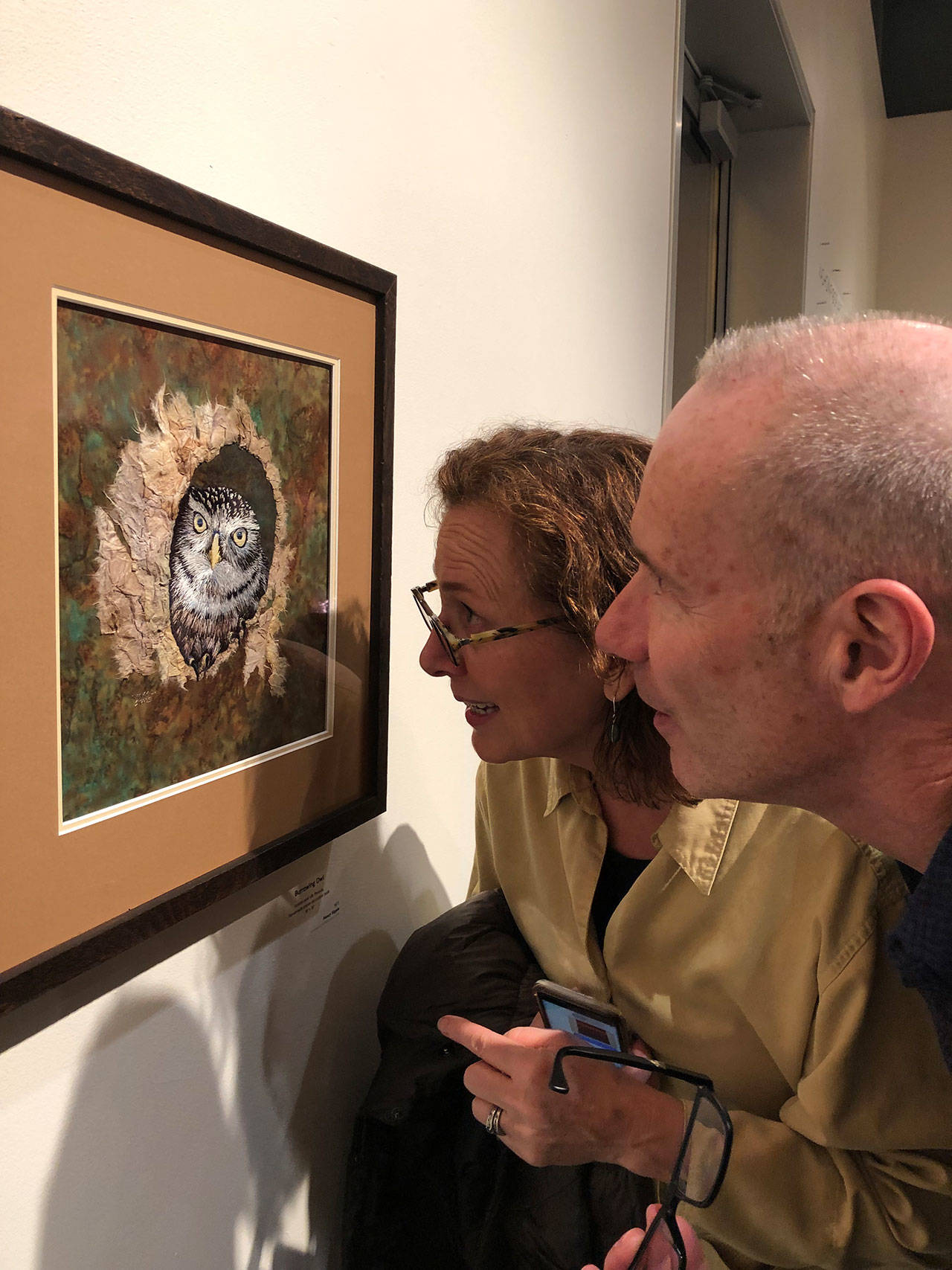 Two art lovers examine Nancy Sipple’s work, “Burrowing Owl,” at Vashon Center for the Arts (Tom Hughes Photo).