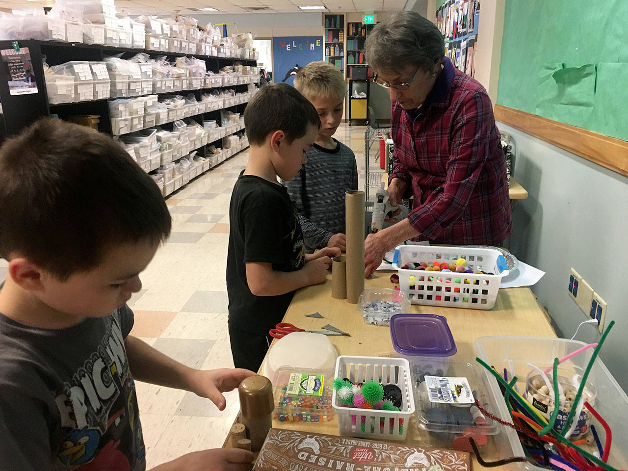 Diane Brenno, stationed at her crafts table outside a Chautauqua Elementary School classroom, wields her glue gun as Niccolo and Teodoro Kuzma and Logan Brenno work on their creations (Elizabeth Shepherd Photo).