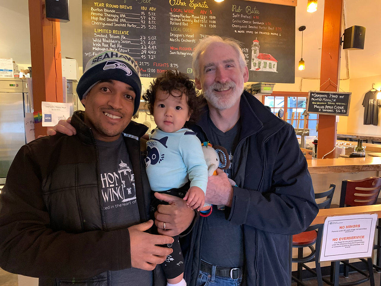Baynody Méndez Jiménez holds his son as his father-in-law, Cliff Goodman, poses with them for a portrait at Vashon Brewing Community Pub last month. (Kevin Opsahl/Staff Photo)