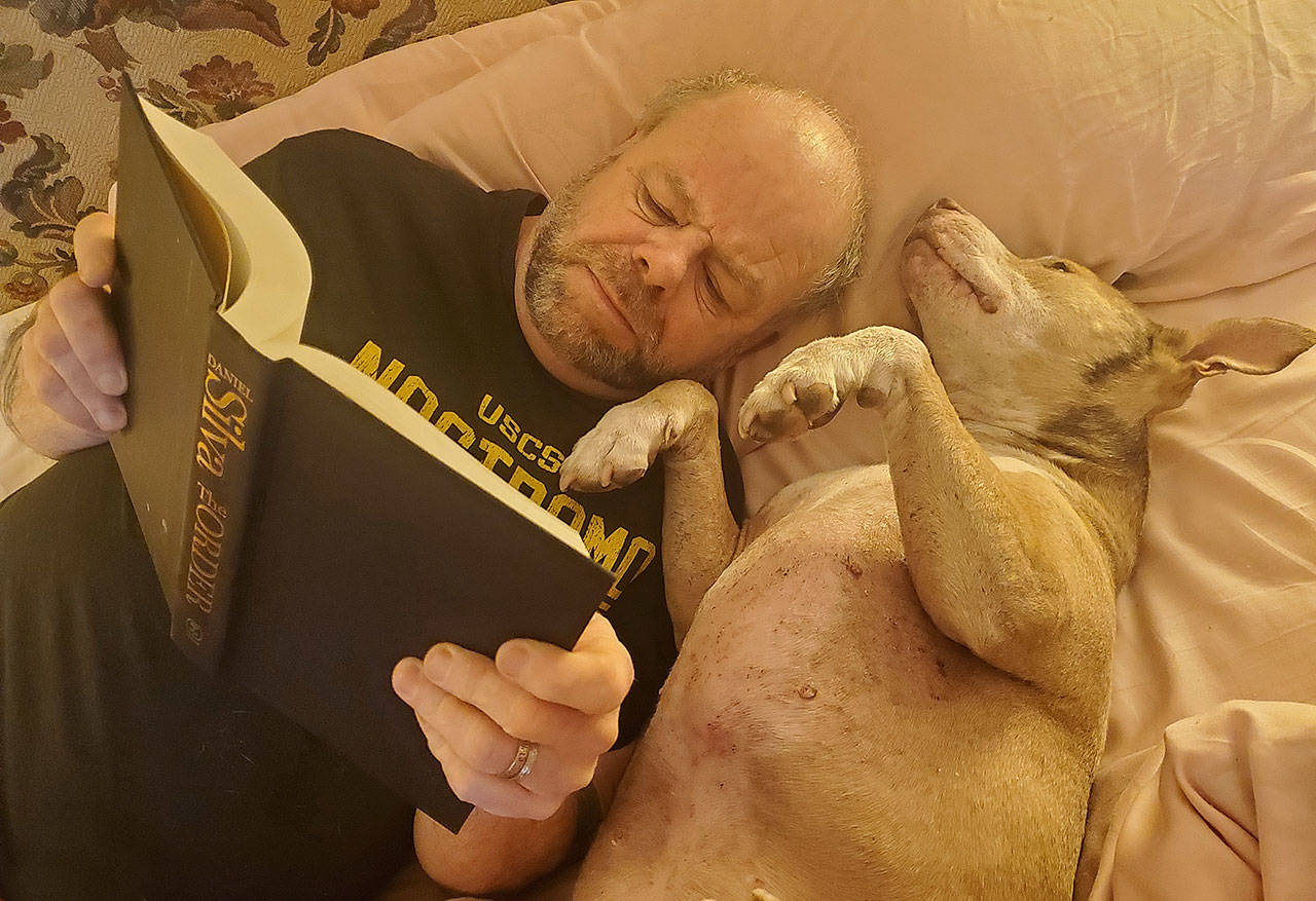 Phil Clapham, reading and dreaming, with a trusty friend by his side (Courtesy Photo).