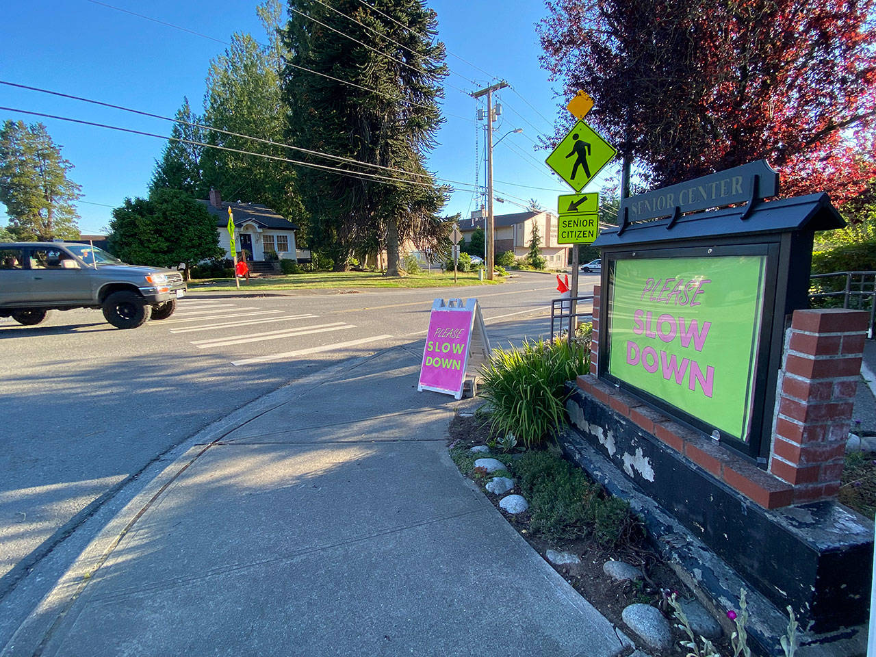 Signs in front of Vashon’s Senior Center warn drivers to slow down as they approach the intersection of Bank Road and 100th Ave. S.W. Bright orange crossing flags for pedestrians have also been installed at the intersection (Tom Hughes Photo).