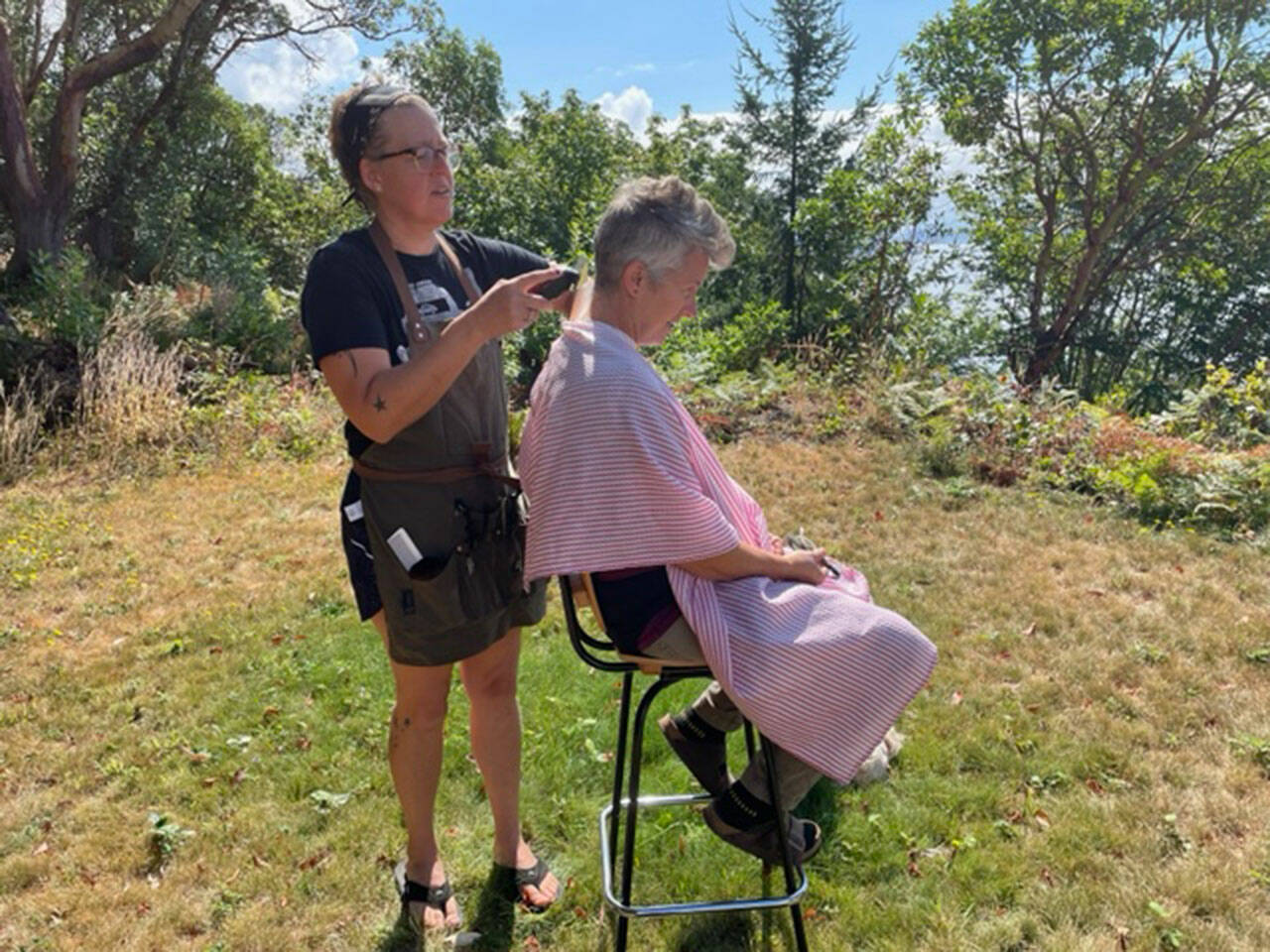 (Photo Courtesy Tara Morgan) Tara Morgan of CMon Barber cuts the hair of islander Denise Paquette at her property on Maury Island.
