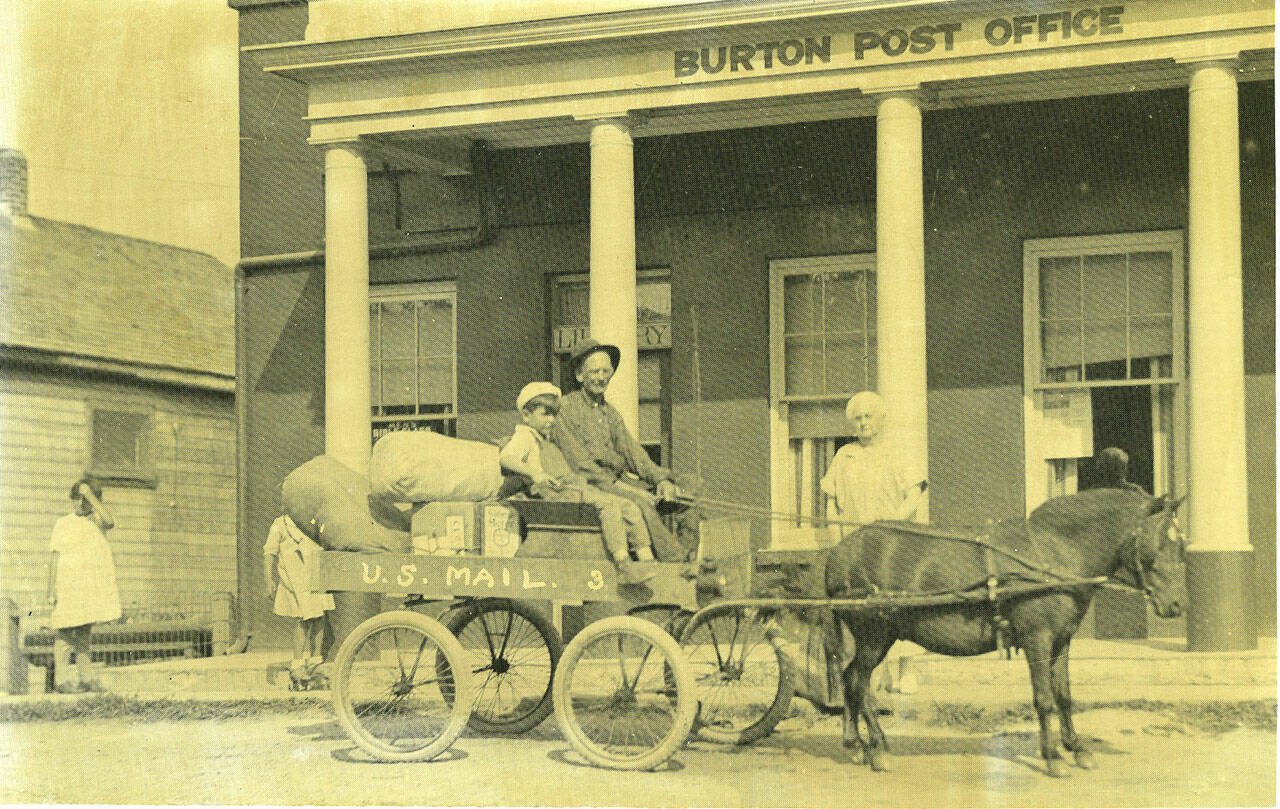 (Photo Courtesy Vashon Heritage Museum) Amos Cummings delivered mail each day between the Burton Post Office and the Burton Dock with his mail cart pulled by the pony, Shamis. In this photograph, taken after 1921 when the post office was built, Burton Postmistress Augusta Hunt stands behind Shamis, and a young Coy Meredith sits beside Amos.