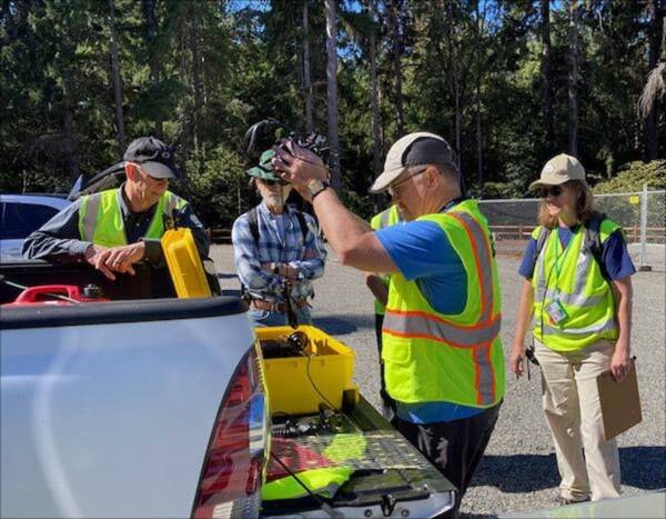 ACS Coordinator Michael Meyer (center) opens up an equipment cache at a radio training class that took place last September in the Dockton trails area. The group recently practiced at Island Center Forest on March 25 (Sharon Danielson Photo).