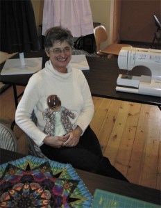 Nancy Sipple sits among pieces she’s created. On her lap is her doll Patsy