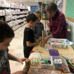 Diane Brenno, stationed at her crafts table outside a Chautauqua Elementary School classroom, wields her glue gun as Niccolo and Teodoro Kuzma and Logan Brenno work on their creations (Elizabeth Shepherd Photo).