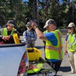 ACS Coordinator Michael Meyer (center) opens up an equipment cache at a radio training class that took place last September in the Dockton trails area. The group recently practiced at Island Center Forest on March 25 (Sharon Danielson Photo).