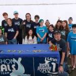 Saffron Hinz, seated center (white sweatshirt) was surrounded by her Vashon Seals teammates and coach Randy Turner (kneeling, on right) at her signing ceremony to swim for Macalester College (Courtesy Photo).