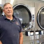 Dennis Morrow, a Port Orchard resident, is one of the co-owners of Vashon Laundry - pictured here next to some of the new washers at the business (Alex Bruell / The Beachcomber Photo).