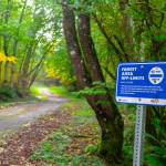 A trail sign in the Maury Island Natural Area, 2023. The sign reads: FOREST AREA OFF-LIMITS. THIS AREA LIES WITHIN THE TACOMA SMELTER PLUME. SOILS MAY CONTAIN HARMFUL LEVELS OF ARSENIC AND LEAD. PROTECT YOUR HEALTH AND STAY ON THE MAINTAINED TRAIL (Photo by Terry Donnelly).