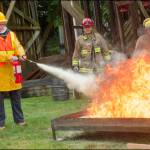 Practical Training with Fire Extinguishers: New CERT volunteers Joni Larned (left) and Kate OHare (with extinguisher) buddy up to get experience using a fire extinguisher. Vashon Island Fire & Rescue (VIFR) Captain Josh Munger (left rear) and volunteer firefighter Jim Wescott (right rear) instructed the volunteers at the VIFR training ground.