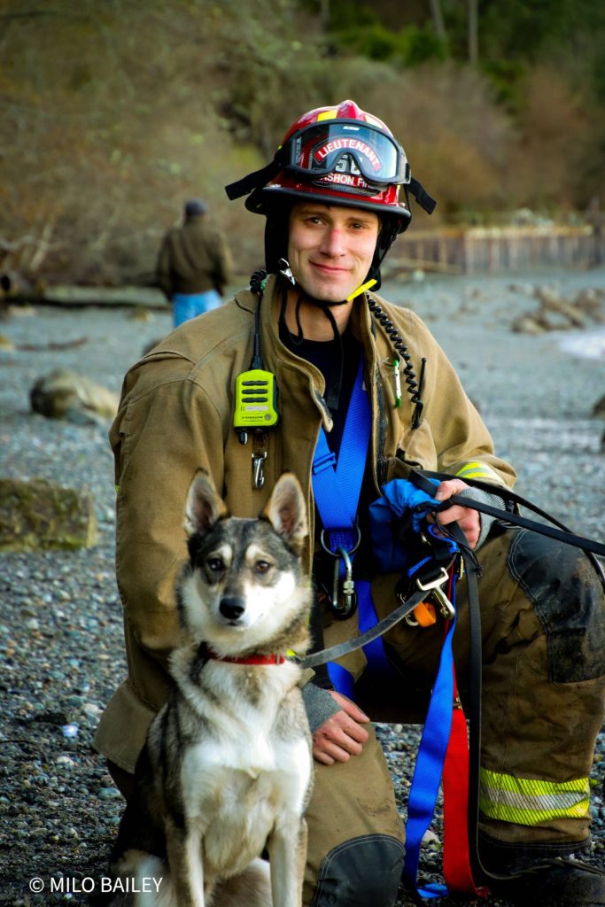 Photo by Milo Bailey
Vashon Island Fire and Rescue Lieutenant Ben Steele kneels next to Kirby, the dog that Steele and his VIFR crew rescued from a cliff at KVI beach last week.