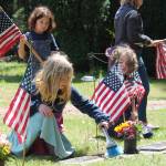 Tom Hughes Photo
Members of Vashons Cub Scout Pack 275, Luna Cekosh (kneeling, left), Hazel Ecevedo (standing), and Wilfred Gogarten (right) place American flags on the graves of veterans at Vashon Cemetery.