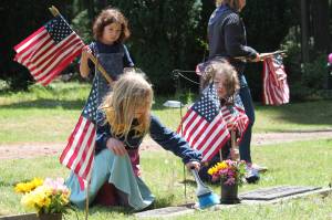 Tom Hughes Photo
Members of Vashons Cub Scout Pack 275, Luna Cekosh (kneeling, left), Hazel Ecevedo (standing), and Wilfred Gogarten (right) place American flags on the graves of veterans at Vashon Cemetery.