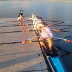 Ben Steele photo
Rose Ely, Gwen Tomlinson, Ren Colvos, Emily Rock, and Alekos Dalinis sit with rows at the ready. Coach Delany Steele crouches on the pier nearby.