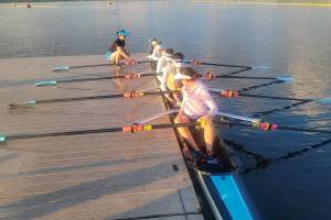 Ben Steele photo
Rose Ely, Gwen Tomlinson, Ren Colvos, Emily Rock, and Alekos Dalinis sit with rows at the ready. Coach Delany Steele crouches on the pier nearby.