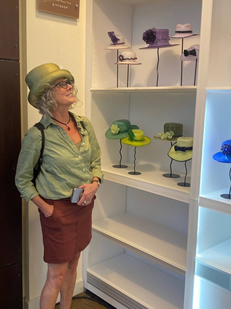 Hatmaker Laura Clampitt admires a selection of glass hats by Brian Brenno at Vashon Center for the Arts. (Lynann Politte photo.)
