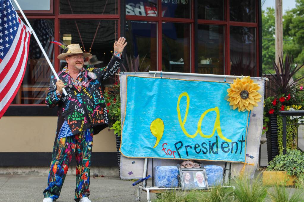 Islander Matt Beursken waves to drivers in Vashon town, sporting a colorful jacket and an American flag. (Aspen Anderson photo.)