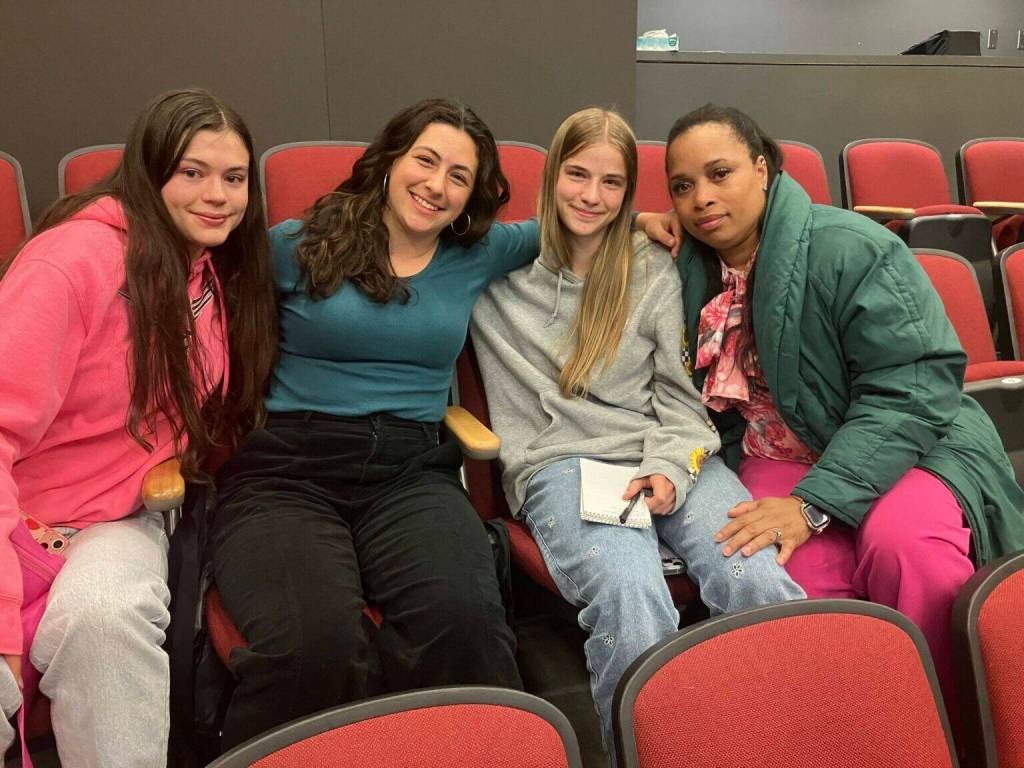 (Left to right) Alana Bass, Amelia Medeiros, Annabelle Moeckel, and school nurse and track coach Brandi Greenidge sit together after the school board meeting. In an emotional appeal, the three students urged the board not to cut Greenidges job. (Elizabeth Shepherd photo)