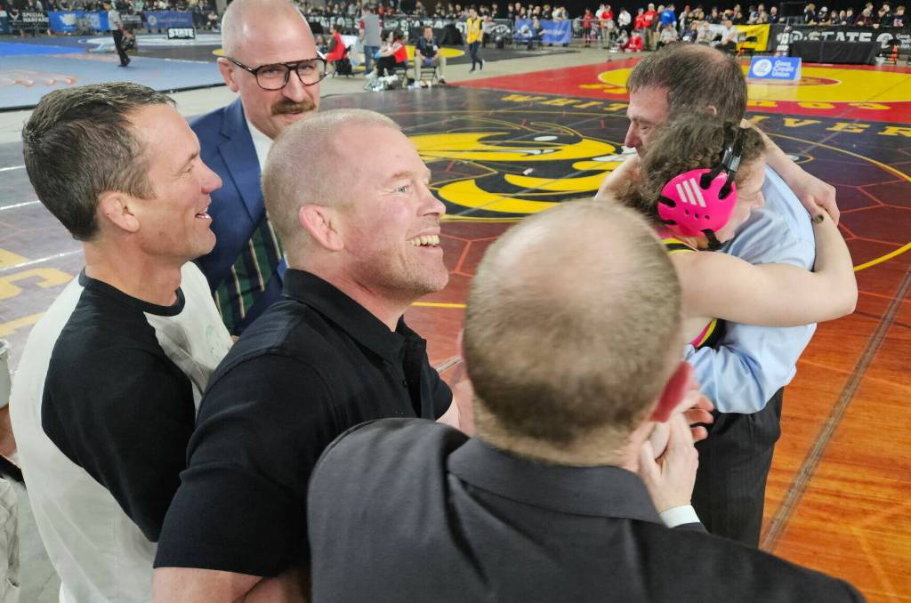 Junior Lena Puz embraces her father and coach, Tony Puz, just after winning her final match and clinching the state championship at the Mat Classic. Also in the photo, from left to right: Coaches Per-Lars Blomgren, Jan Martin Nielsen, Anders Blomgren, and Stephen Murphy. (Jim Meyerhoff, WIAA photo)