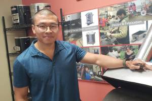 Courtesy photo
Jeremy Su stands next to the shea nut roaster BDL recently designed. On the shelves behind him are many many of BDL's household stoves.