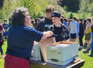 Courtesy photo
English teacher Mandy Davis distributes the book “Minor Poetry” to Liam Bojko and Evan Keller at the seventh grade launch party, while students in the background line up for refreshments.