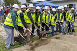 Local and regional leaders ceremonially strike shovels into the dirt at a ground-breaking ceremony for the Vashon-Maury Food Banks new location at the United Methodist Church, as a crowd behind raises apples celebratorily. (Alex Bruell photo)