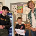 VHS seniors Sky Skiena (left) and Henry Sutherland flank Lewis Goodmansen, a kindergarten student in Manda McCoys class, holding a book inspired by his artwork and list of favorite things. (Courtesy Photo)