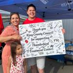 King County Councilmember Teresa Mosqueda and her daughter, Camila stopped by Seattle Indian Health Boards booth at Strawberry Festival. In this photo, Wayne Harvey, development program director of the Health Board, and Mosqueda hold a poster-sized letter to King County, signed by islanders during the festival, thanking the county for its support of the new 92-bed Thunderbird Treatment Center on Vashon. (Tom Hughes photo)