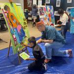 Wade Antonio Colwell helps a visitor paint Mi Cariño during Día del Niño. Wade took over after Colwells passing to ensure that this event could continue to be held to showcase his mothers art.