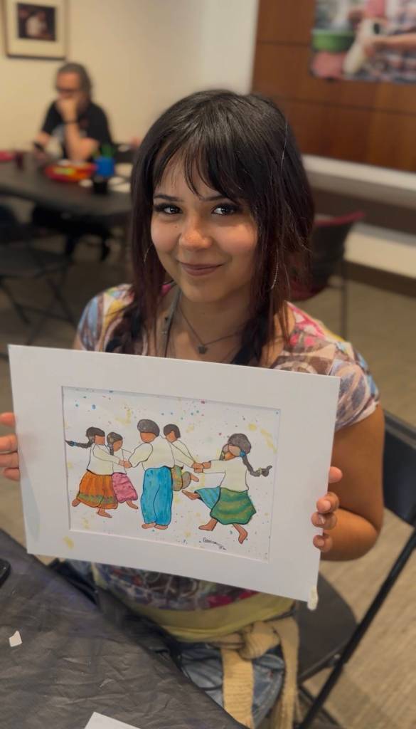 Colwells granddaughter, Kamila, holds up a painting by Colwell at Día del Niño.