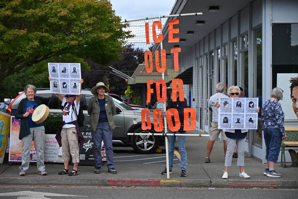 A handful of islanders stand beneath an ICE Out for Good banner during an anti-ICE vigil Saturday, July 25, near Vashons four-way stop. The demonstration was organized by Vashon-Maury Showing Up for Racial Justice. (Kent Phelan Photo)